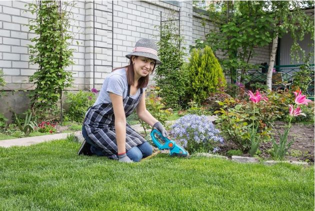 mulher sorridente ajoelhada cuidando do jardim e aproveitando dos benefícios terapêuticos e bem-estar mental